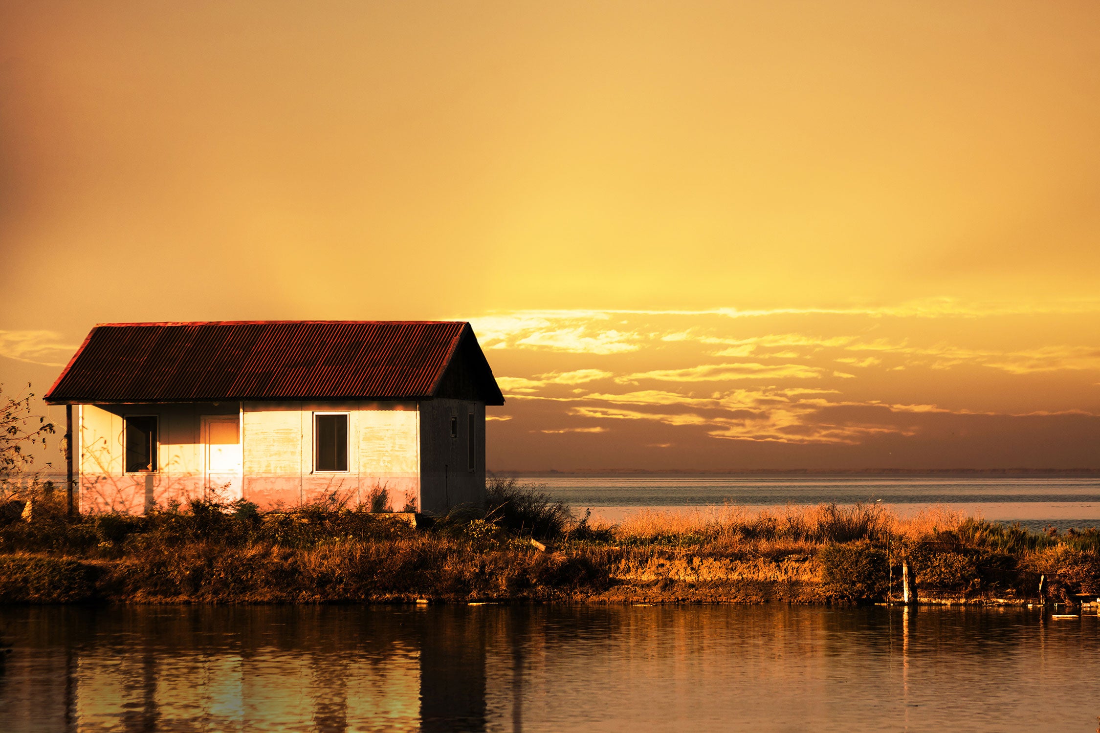 Haus am See bei Sonnenuntergang, Glasbild